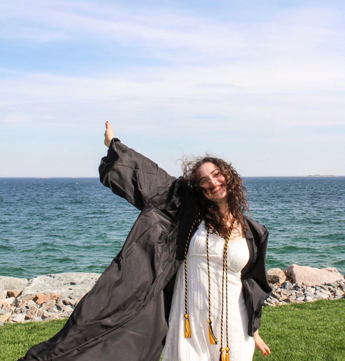 Graduate in cap and gown celebrating by the sea